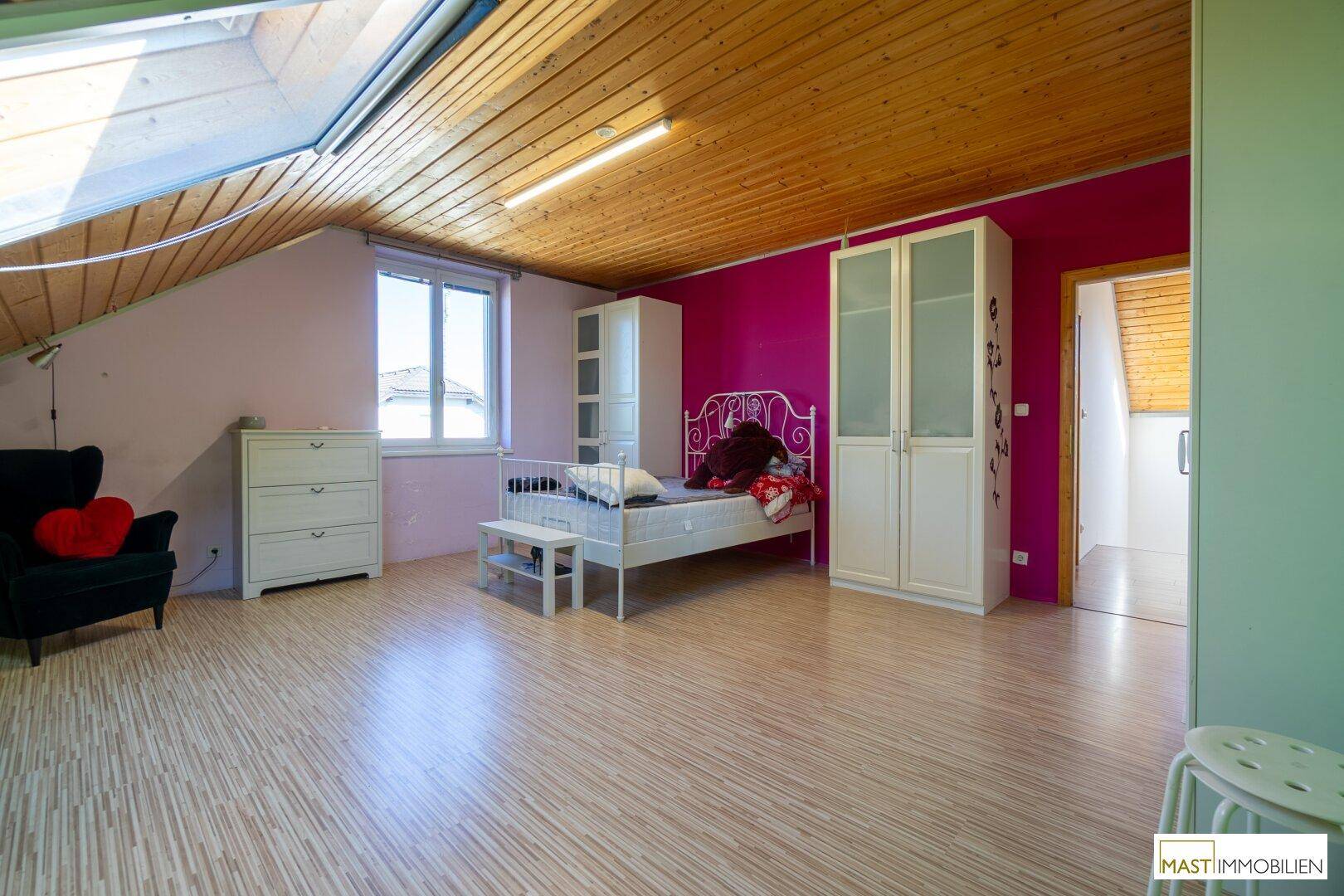 Geräumiges Schlafzimmer im Dachgeschoss mit Holzdecke, Dachfenster und farbigen Wänden.