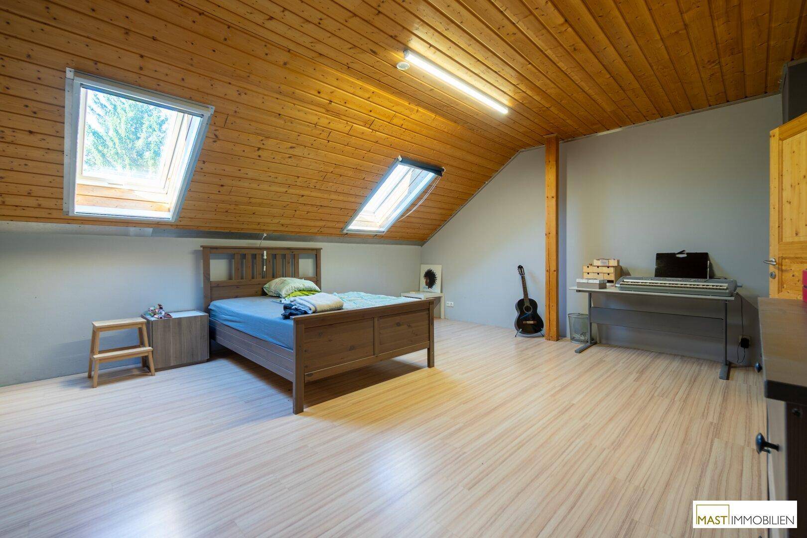 Schlafzimmer im Dachgeschoss mit Holzdecke, zwei Dachfenstern und Laminatboden.