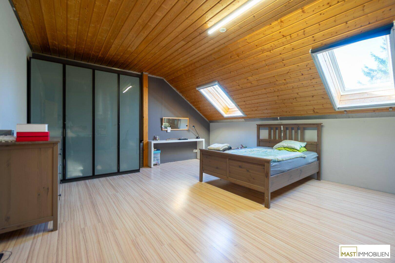 Dachgeschoss-Schlafzimmer mit Holzdecke, Dachfenstern und integriertem Kleiderschrank.