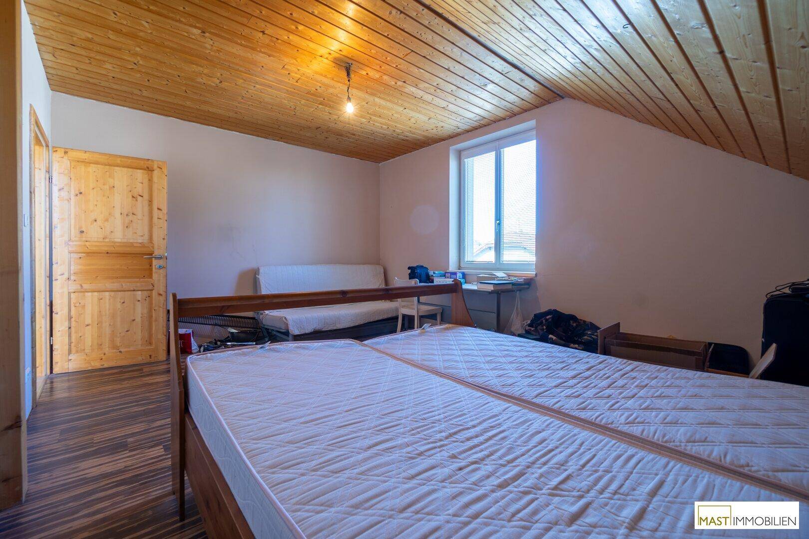 Gemütliches Schlafzimmer im Dachgeschoss mit Holzdecke, Holztür und Fenster.