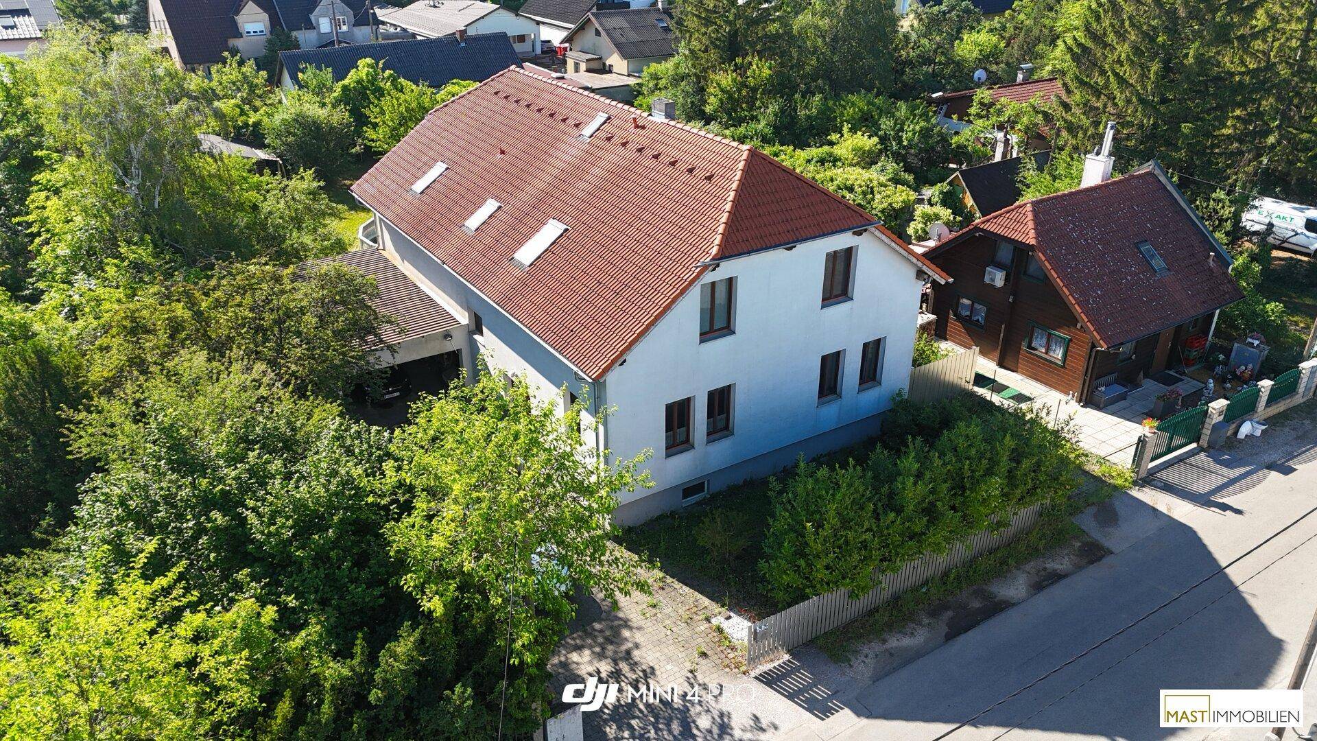 Luftaufnahme eines Einfamilienhauses mit rotem Ziegeldach, umgeben von üppigem Grün und Bäumen.