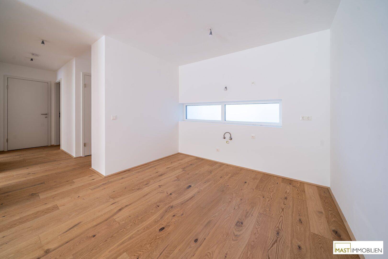 Leerer Raum mit Holzboden und weiß gestrichenen Wänden, vorbereitet für eine Küche.