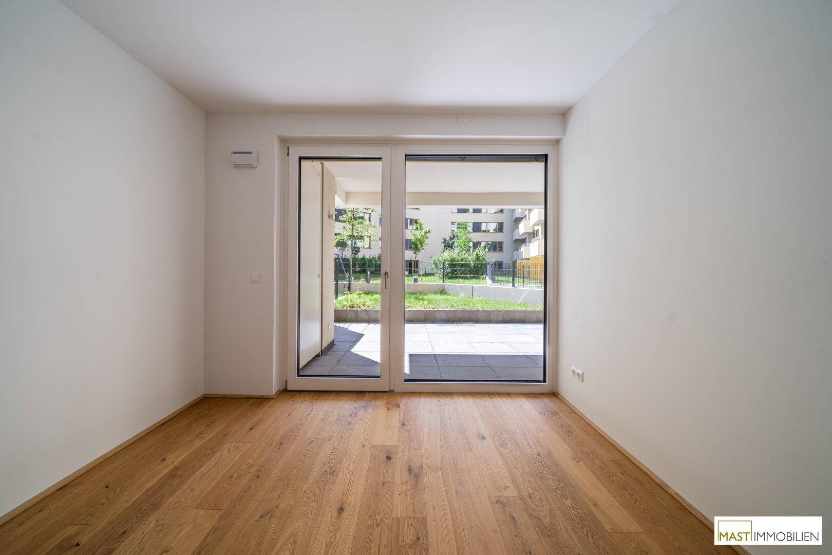 Geräumiges Schlafzimmer mit Holzboden und großen Fenstern mit Blick ins Grüne.