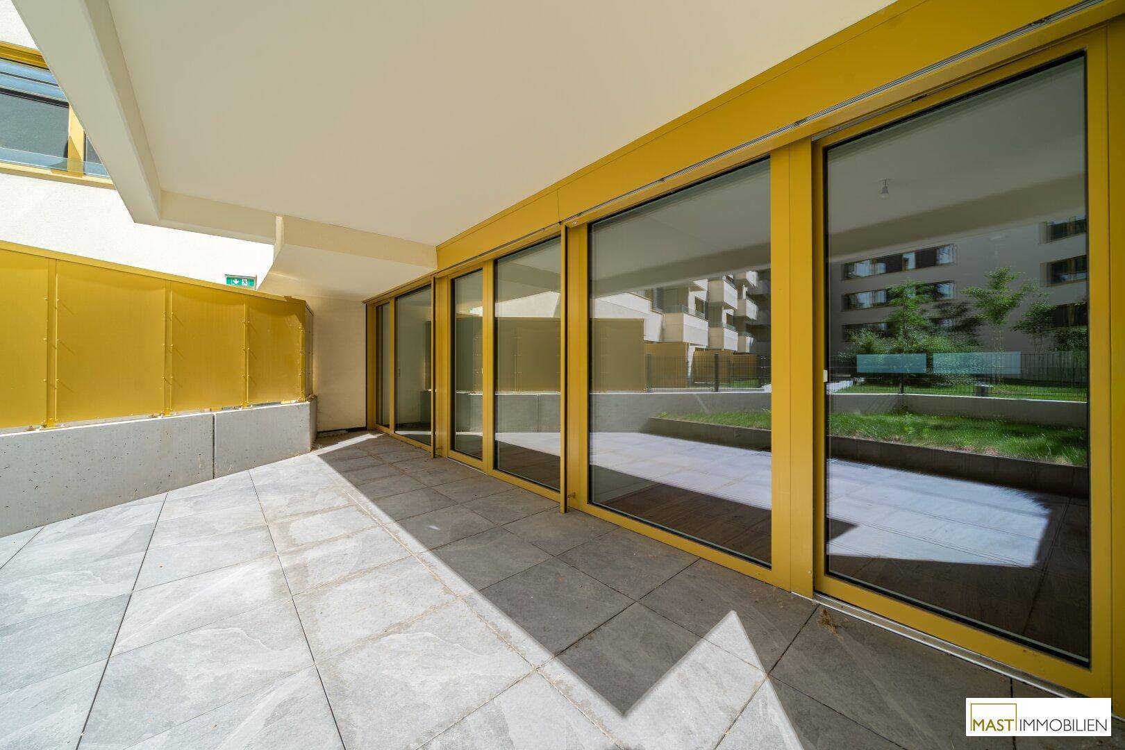 Geräumige, geflieste Terrasse mit großen Glasschiebetüren zum Innenbereich des Gebäudes.