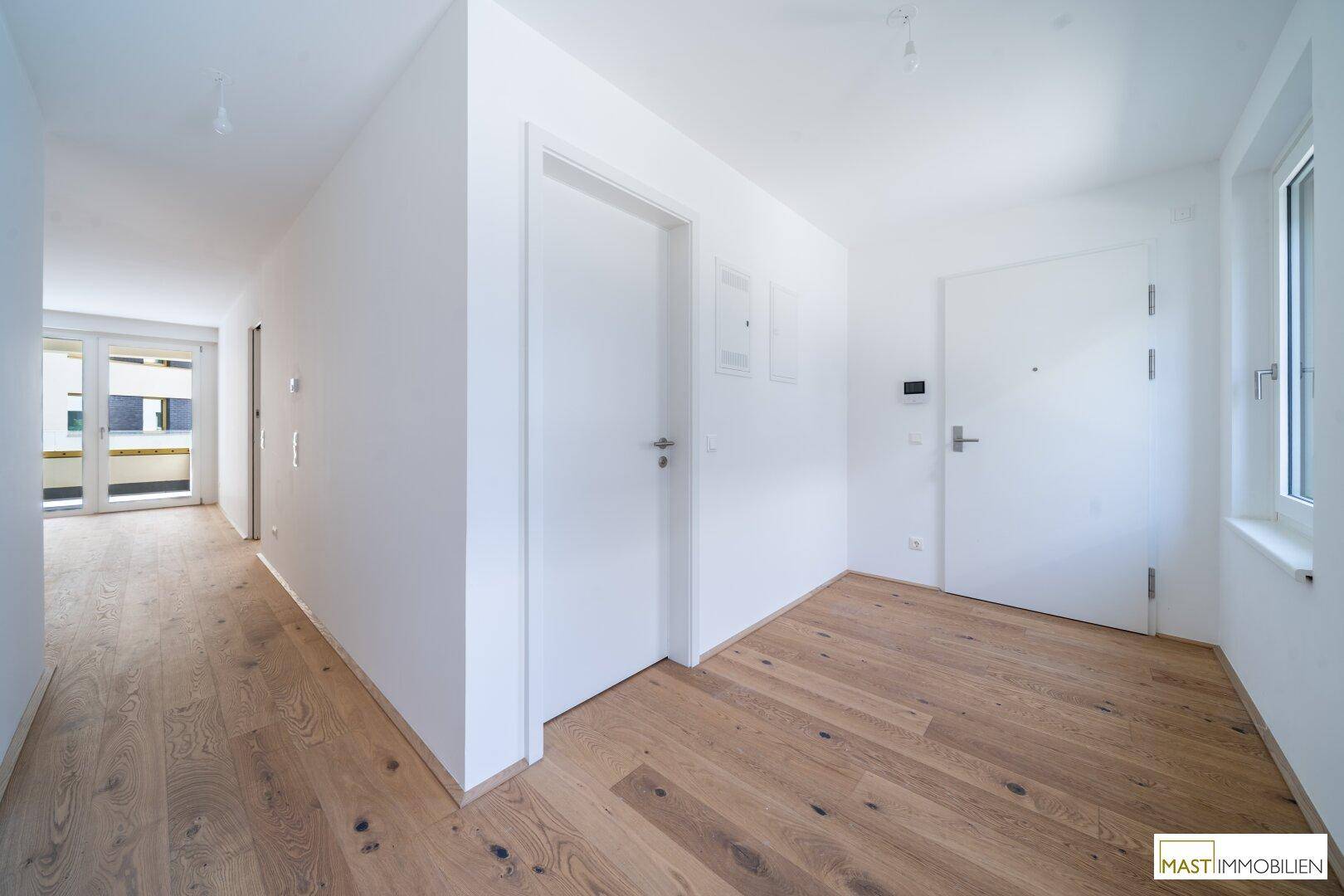 Heller Flur mit modernem Holzparkett und weißen Wänden, der zu verschiedenen Räumen führt.