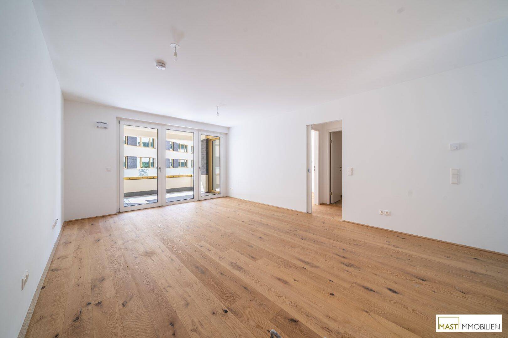Heller Wohnbereich mit Eichenparkett und großen Glasfronten, die Zugang zu einem Balkon bieten.