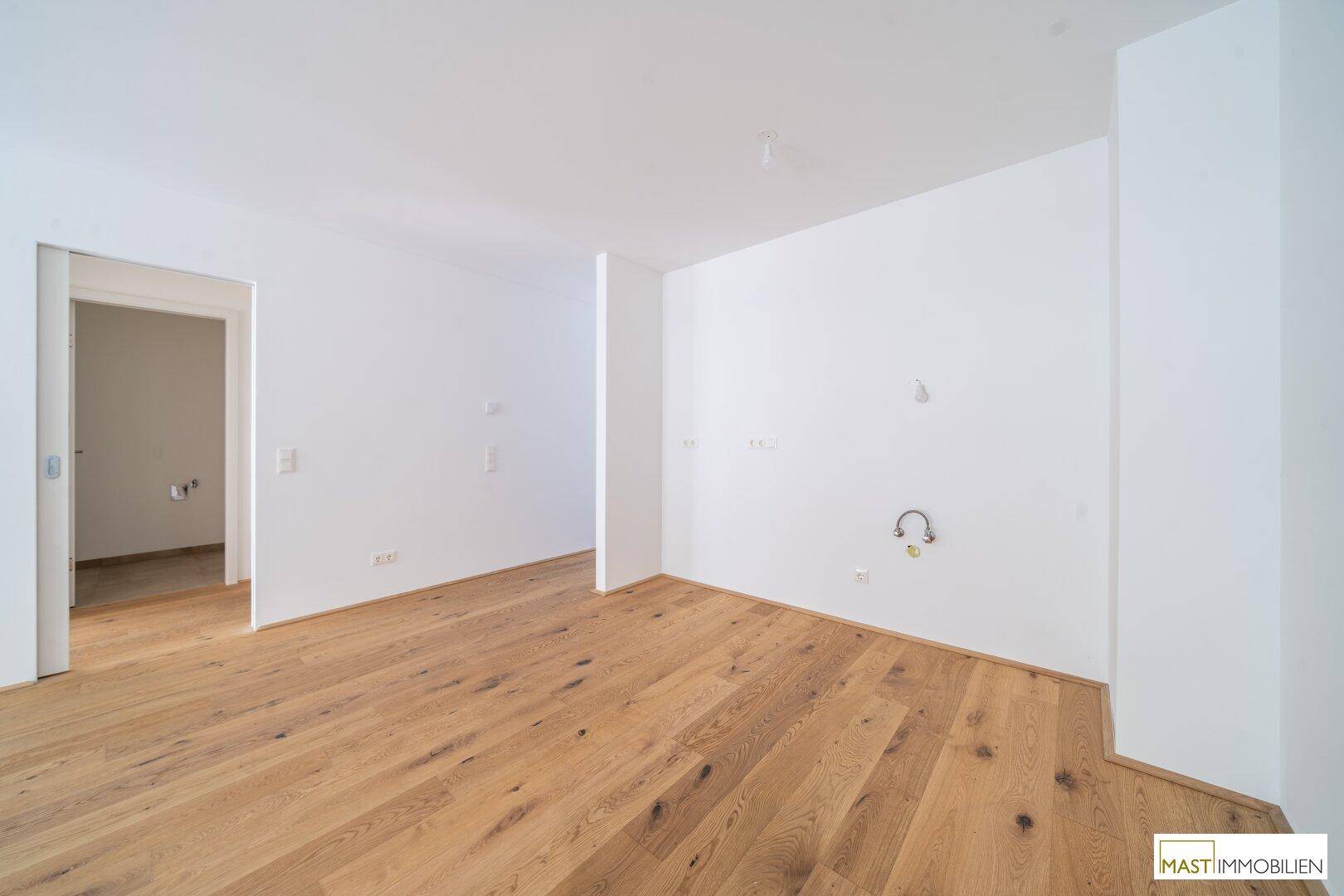 Leerer Küchenbereich mit Holzparkett und Anschlüssen für eine moderne Einbauküche.