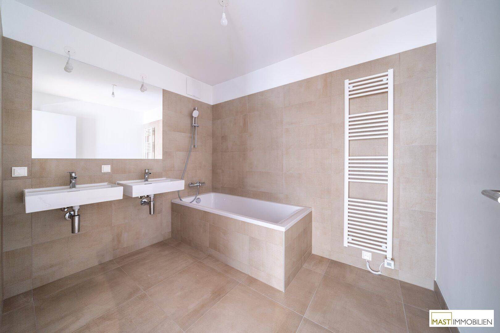 Modernes Badezimmer mit beigefarbenen Fliesen, Doppelwaschbecken, Badewanne und Handtuchheizkörper.