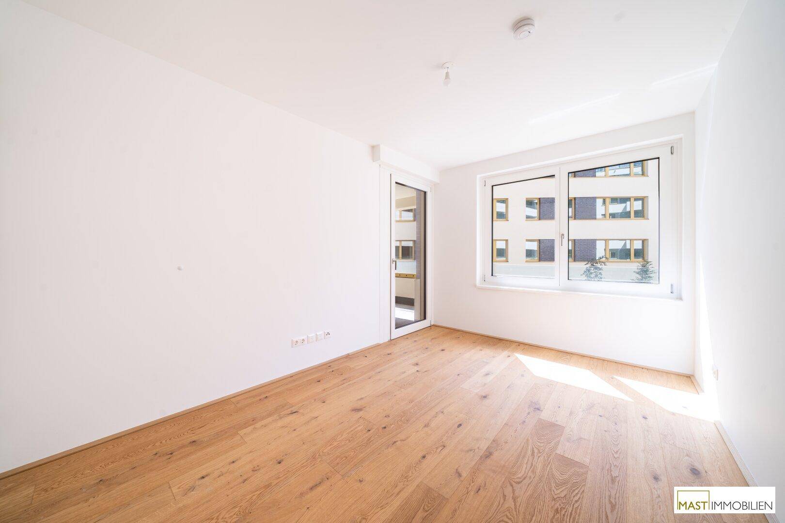 Heller Raum mit Holzparkett und großem Fenster, das viel natürliches Sonnenlicht hereinlässt.