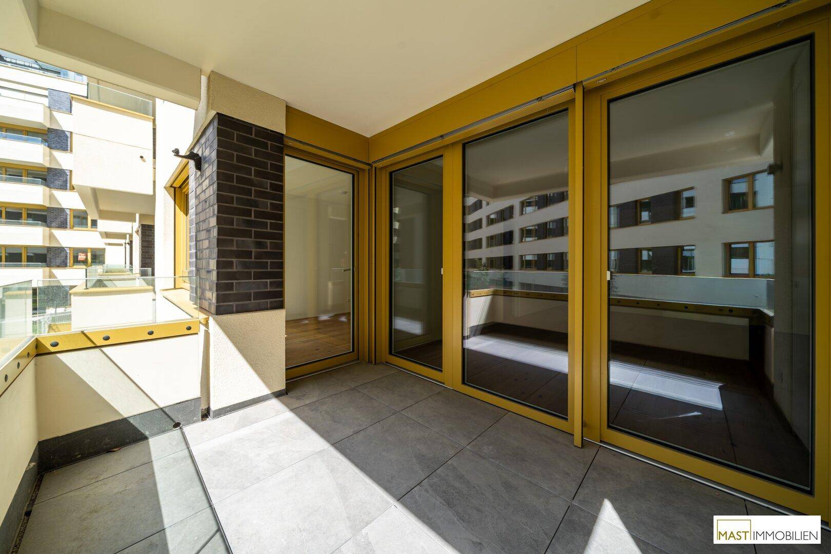 Heller Balkon mit Fliesenboden und großen Glasfronten, die viel Sonnenlicht in die Wohnung lassen.