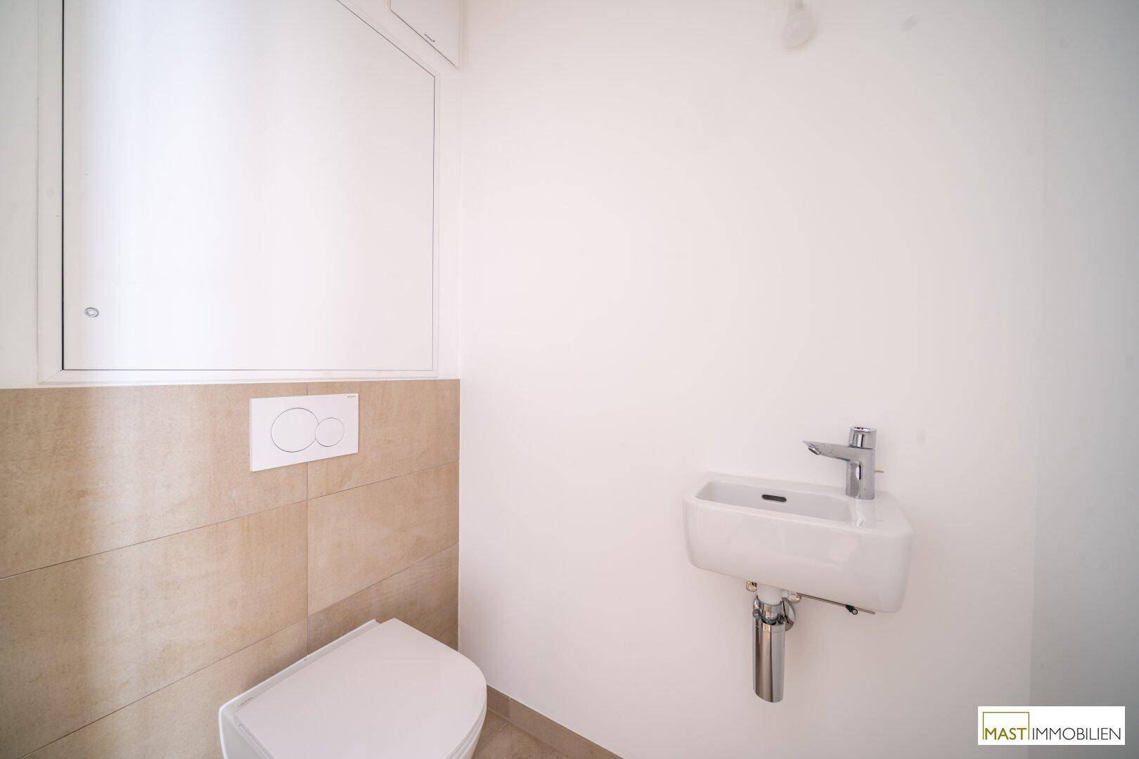 Separates Gäste-WC mit wandhängender Toilette und kleinem Waschbecken, modern gefliest.