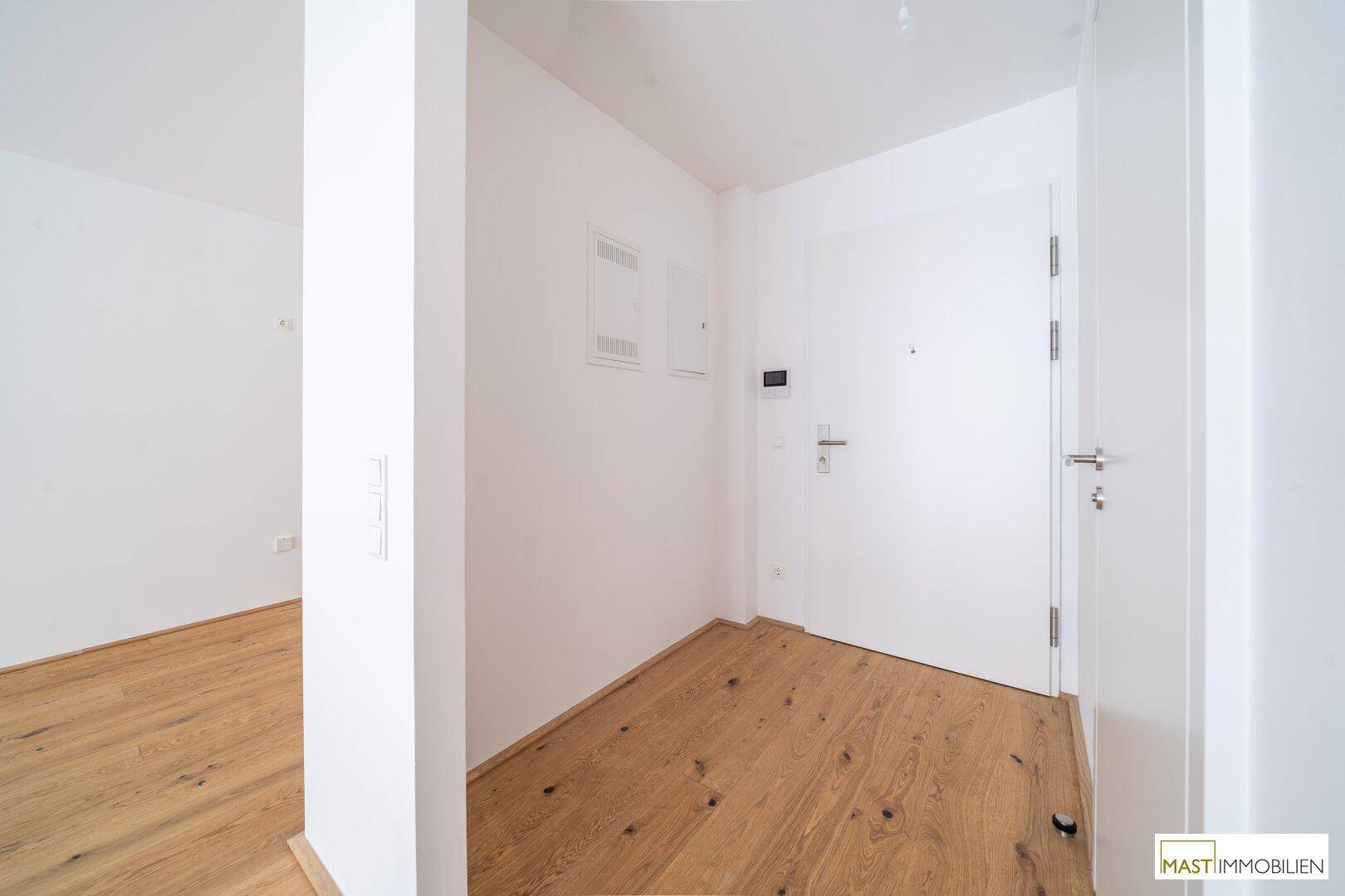 Heller Eingangsbereich mit Holzboden und moderner weißer Eingangstür, die zu den Wohnräumen führt.
