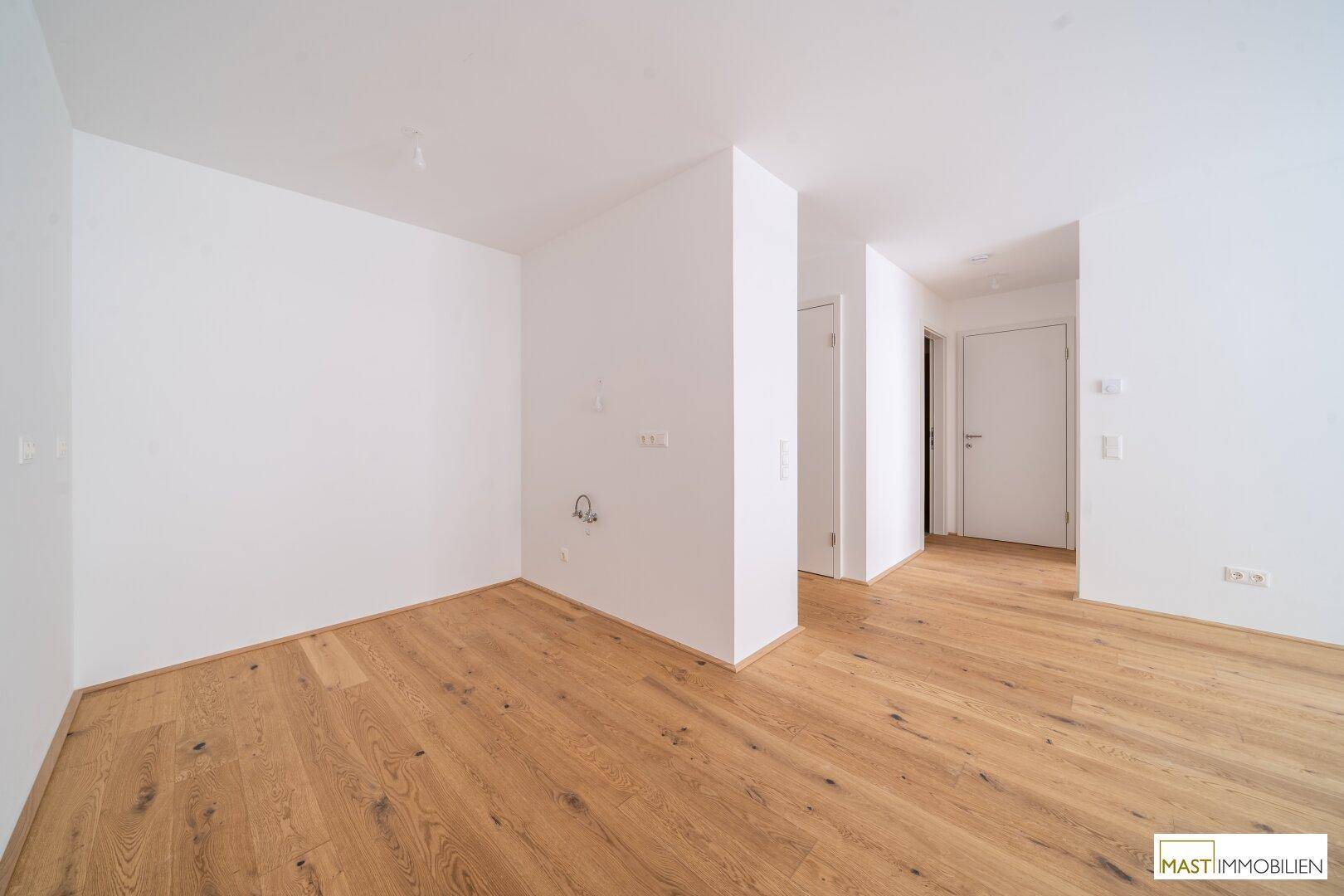 Leerer Raum mit Parkettboden und Anschlüssen für eine Küche, bereit für die Installation.