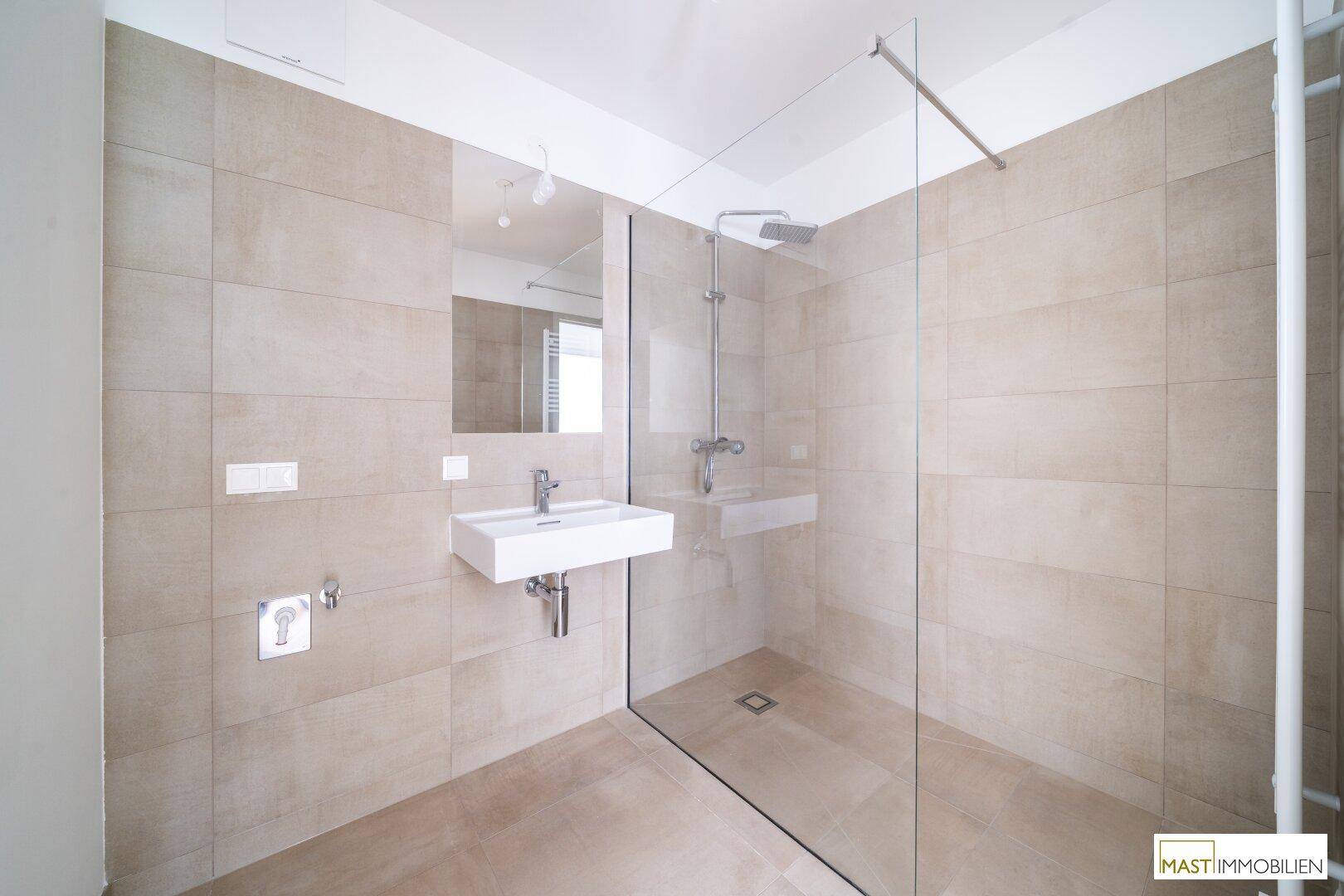 Elegantes Badezimmer mit großformatigen Fliesen, modernem Waschbecken und geräumiger Regendusche.