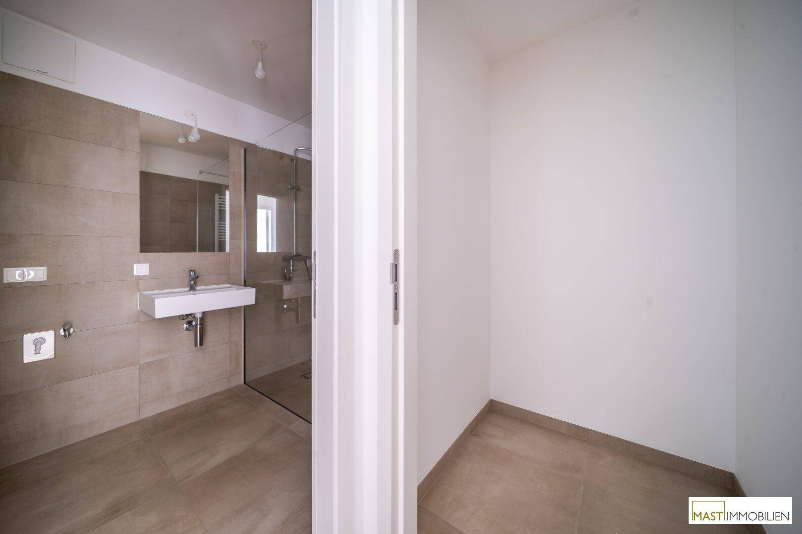 Modernes Badezimmer mit beigefarbenen Fliesen, wandhängendem Waschbecken und einer begehbaren Dusche.