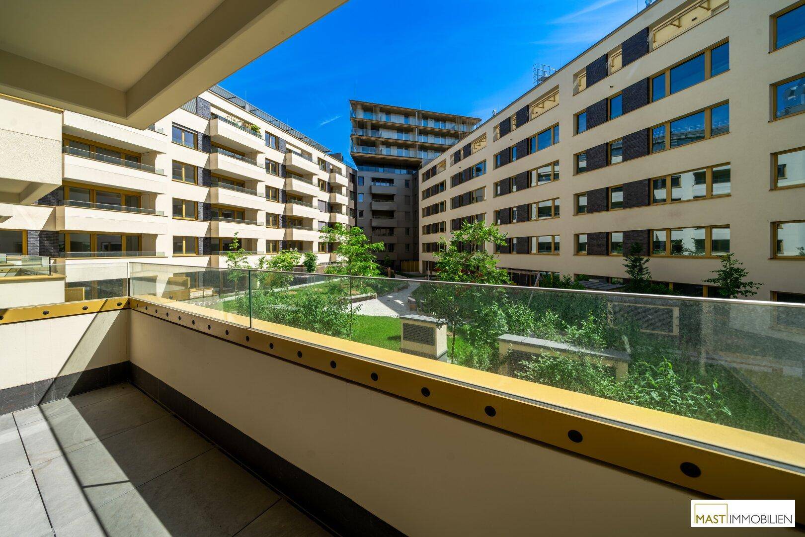 Blick vom Balkon auf einen gepflegten grünen Innenhof, umgeben von modernen Wohngebäuden.