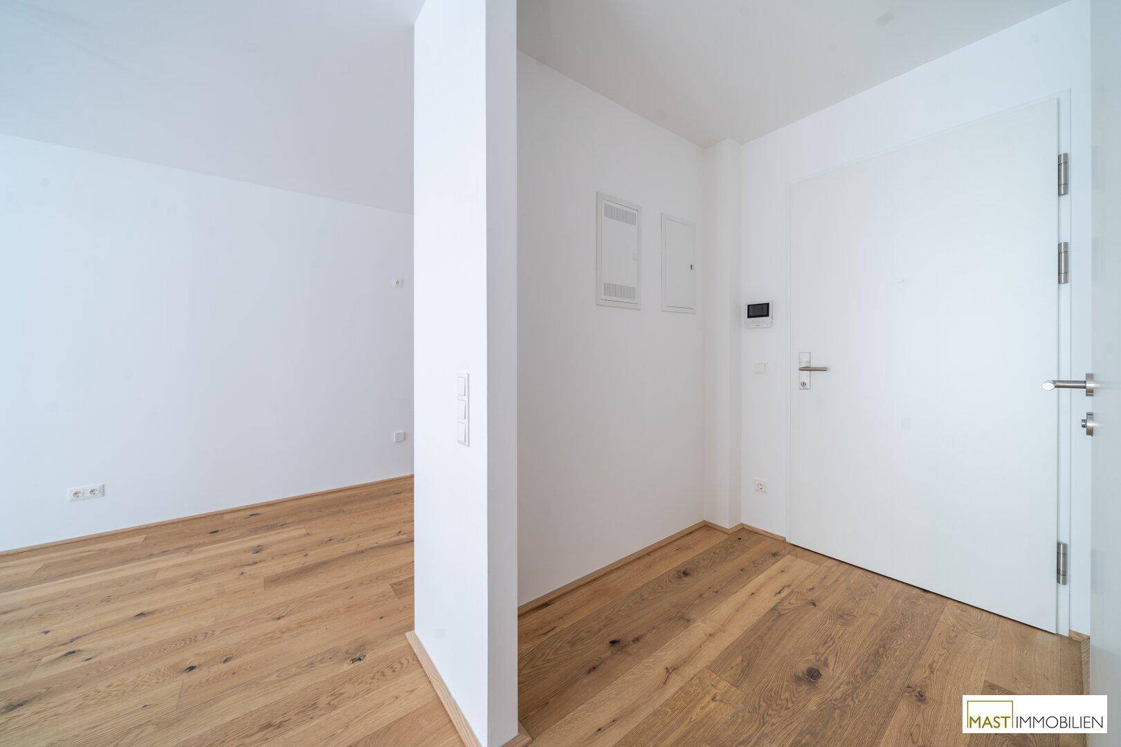 Heller Flur mit Holzboden und weißen Wänden, der zu weiteren Räumen führt.