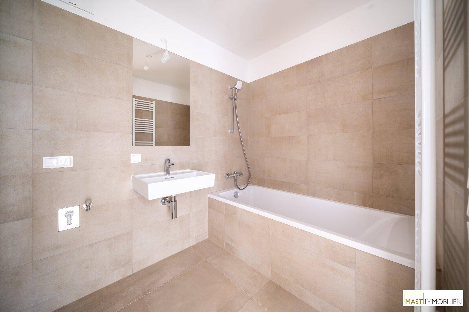 Modernes Badezimmer mit beigefarbenen Fliesen, Badewanne und Waschtisch, in neuwertigem Zustand.