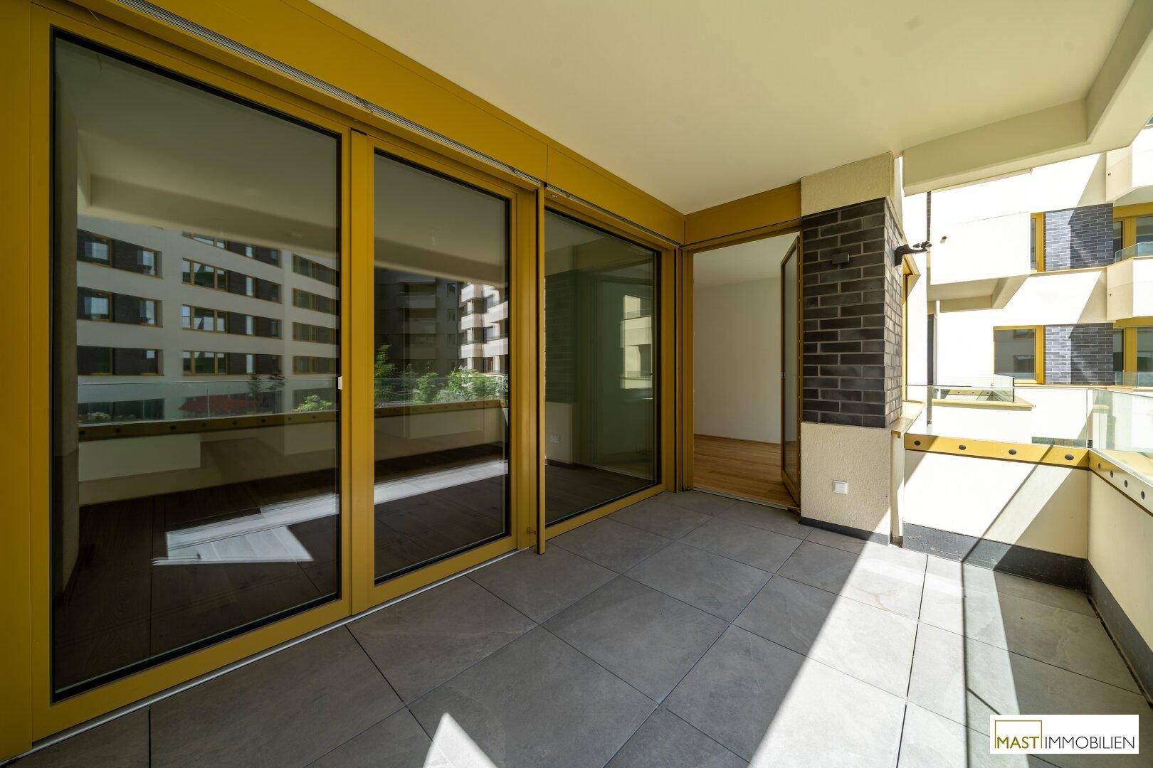 Geräumiger Balkon mit Fliesenboden und Glasbrüstung, bietet viel Platz im Freien.