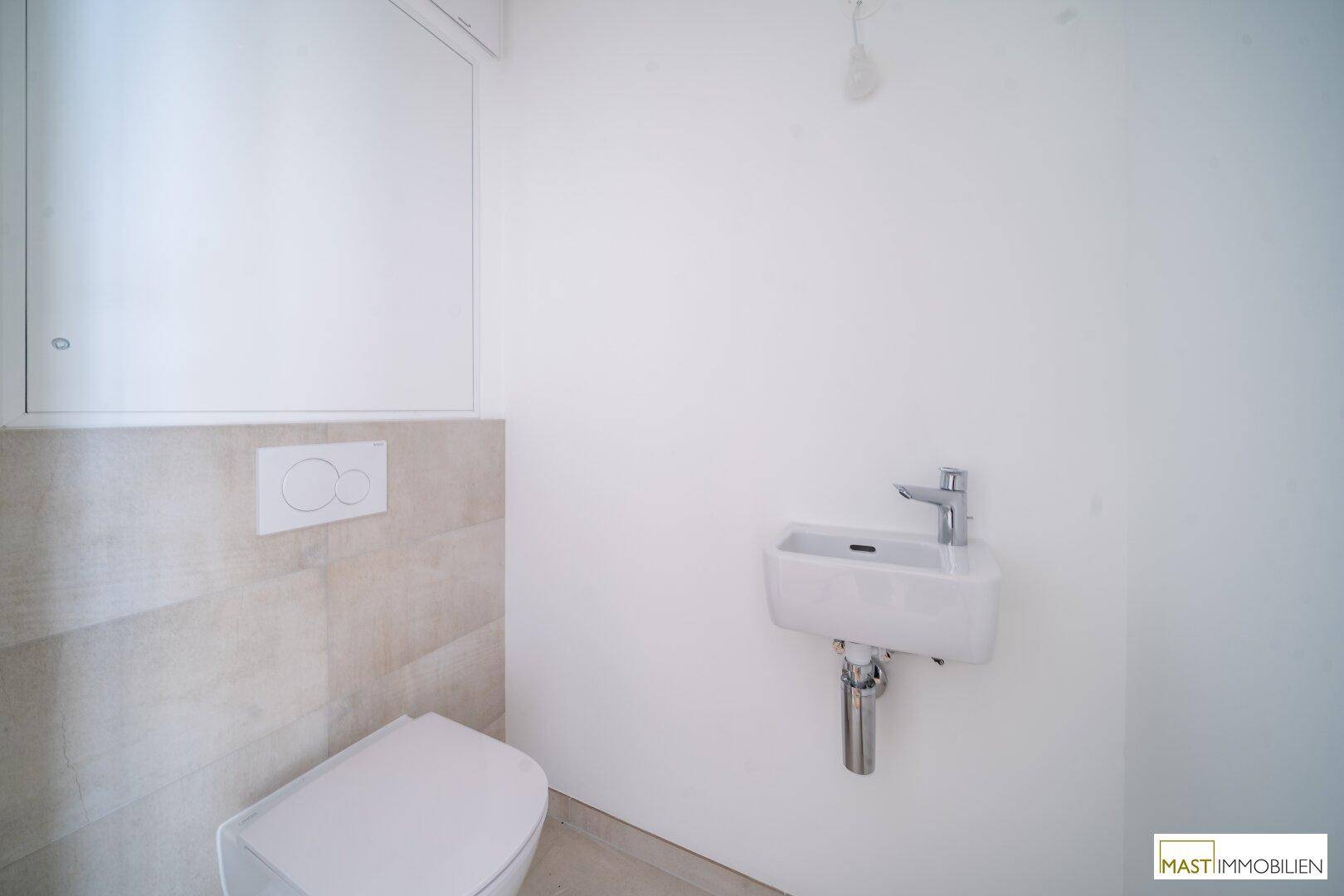Separates Gäste-WC mit wandhängender Toilette und kleinem Waschbecken, modern gefliest.