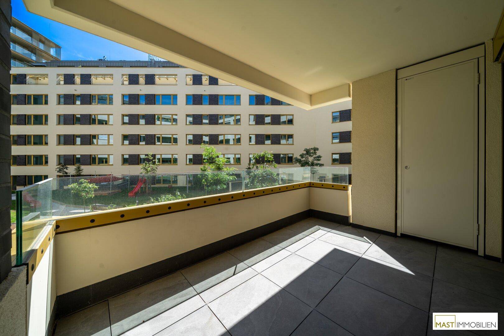 Heller Balkon mit Fliesenboden und Blick auf den gemeinschaftlichen Innenhof der Wohnanlage.