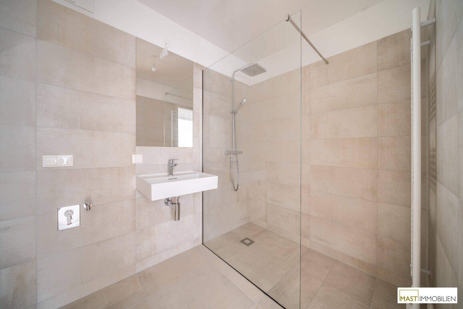 Modernes Badezimmer mit beigefarbenen Fliesen, bodengleicher Dusche und elegantem Wandwaschbecken.