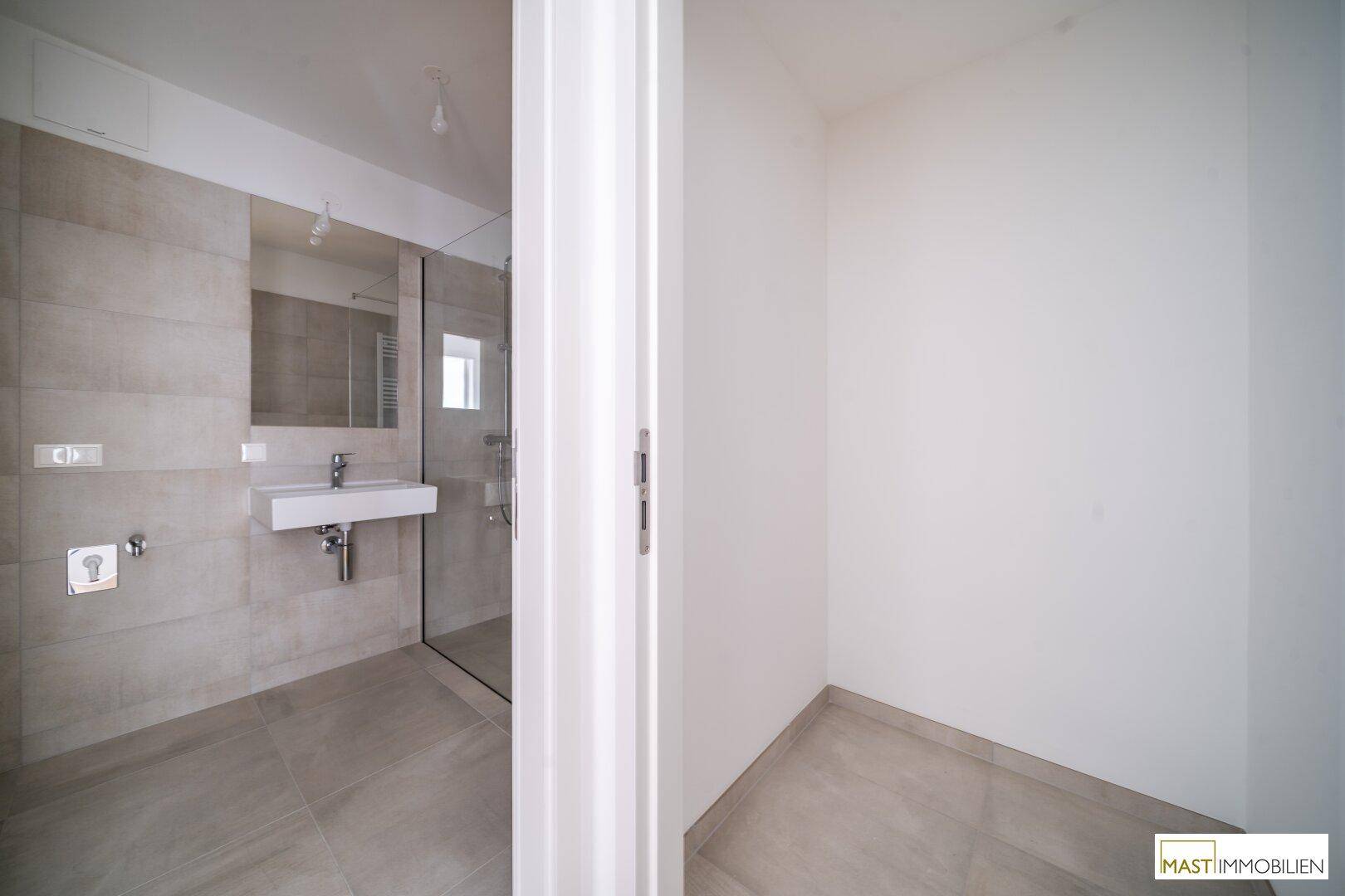 Blick in ein modernes Badezimmer mit angrenzendem, unmöbliertem Raum, der vielseitig nutzbar ist.