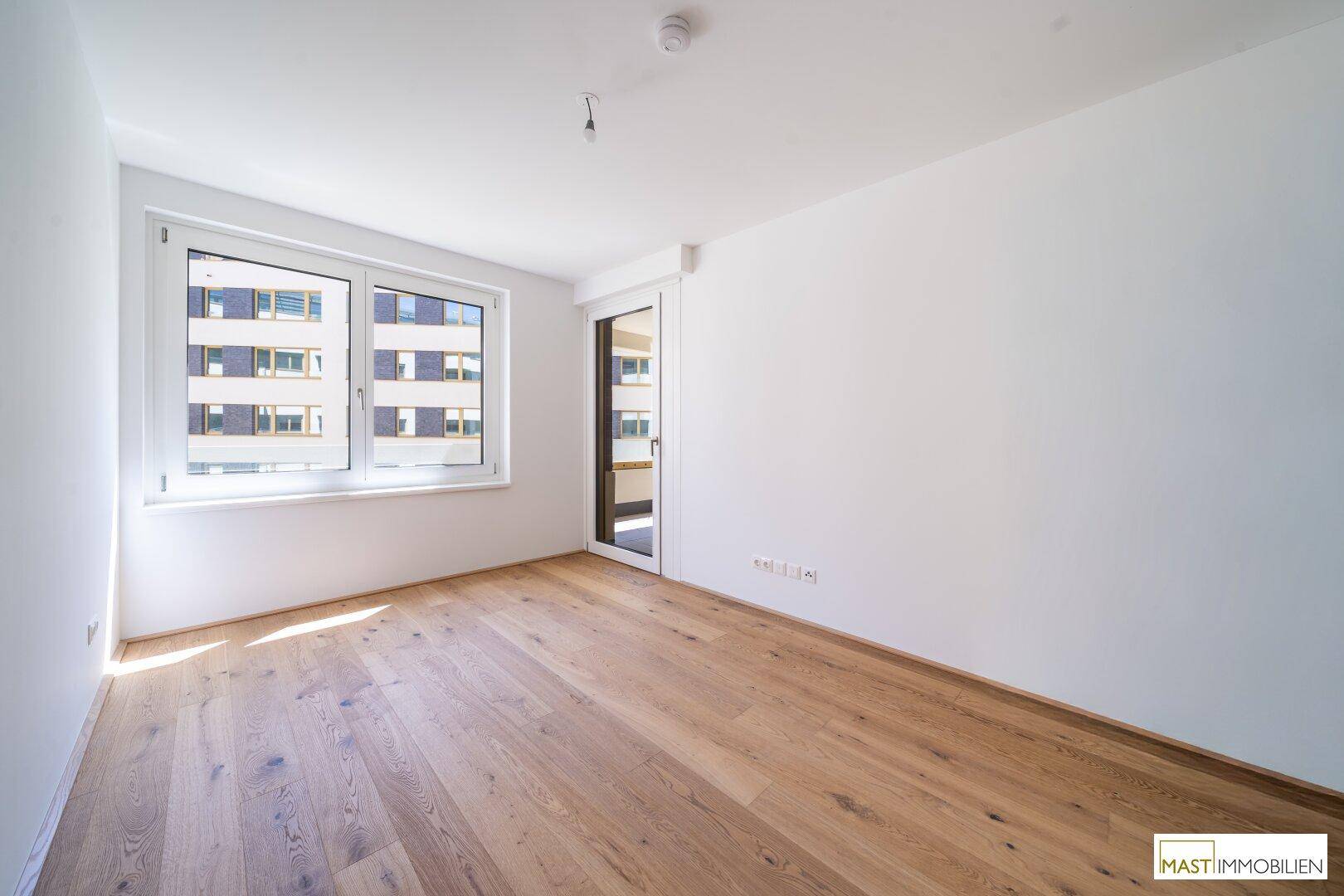 Helles Schlafzimmer mit Holzboden und Fenster, bietet Zugang zu einem Außenbereich und viel Tageslicht.