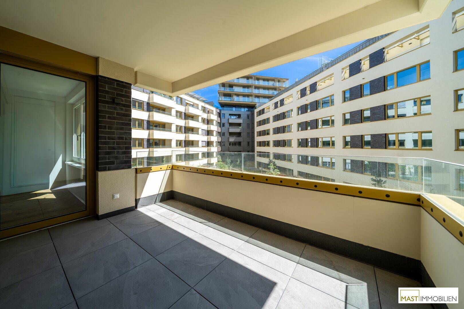 Heller Balkon mit Fliesenboden und Glasbrüstung, bietet einen weiten Blick auf den Innenhof und die Umgebung.