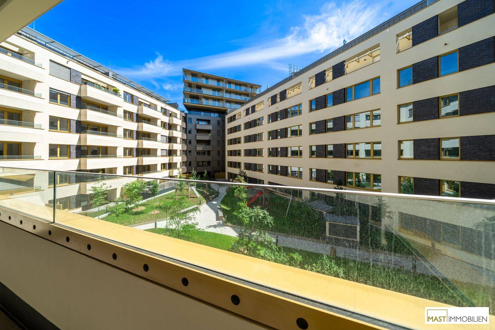 Panoramablick vom Balkon auf den grünen Innenhof mit Spielplatz, umgeben von moderner Architektur.