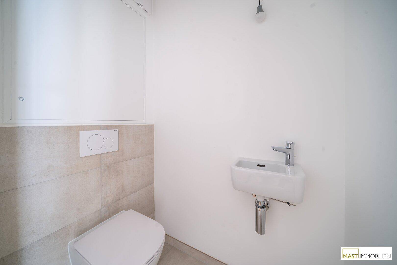 Modernes Gäste-WC mit wandhängender Toilette und kleinem Waschbecken, ausgestattet mit hellen Fliesen.