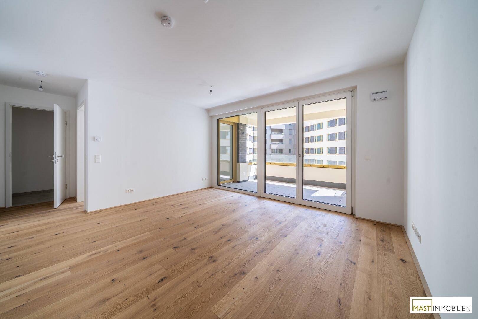 Geräumiges, helles Zimmer mit Echtholzparkett und Zugang zu einem Balkon, ideal für Wohn- oder Schlafbereich.
