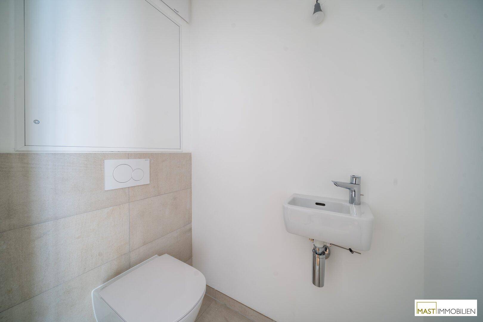 Separates Gäste-WC mit wandhängender Toilette, kleinem Waschbecken und hellen Fliesen.