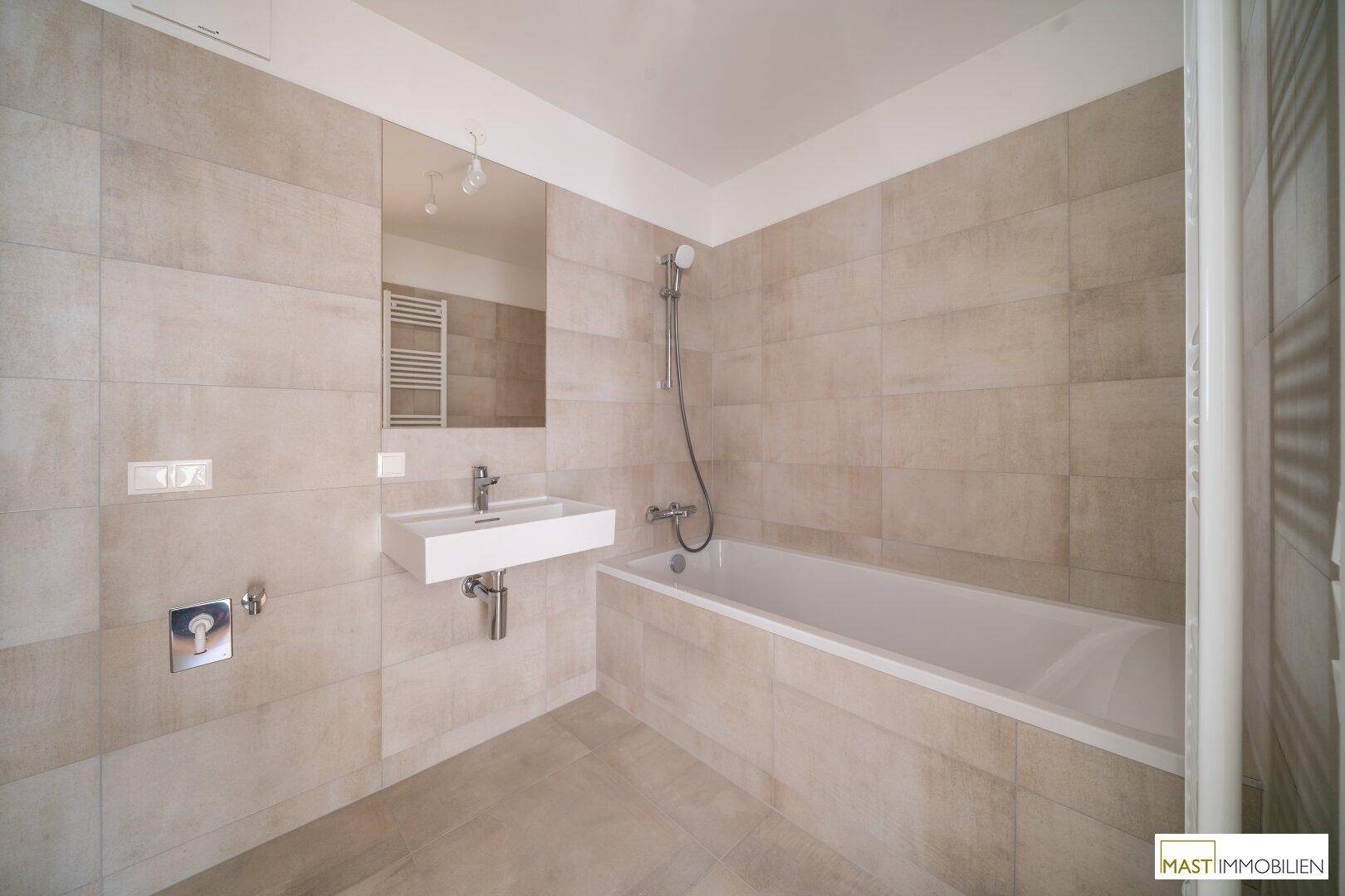 Modernes Badezimmer mit hellen Fliesen, Waschbecken, Spiegel und Badewanne mit Duschfunktion.