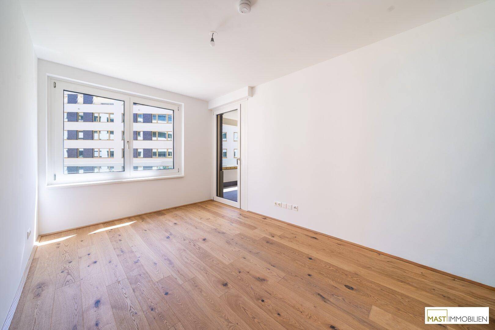Helles Schlafzimmer mit Holzboden und großem Fenster, bietet Zugang zu einem Außenbereich.