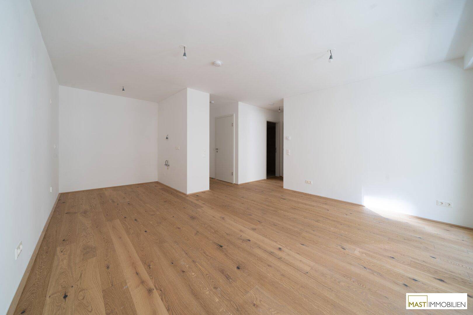 Geräumiges, unmöbliertes Wohnzimmer mit hellem Eichenparkett und weißen Wänden.