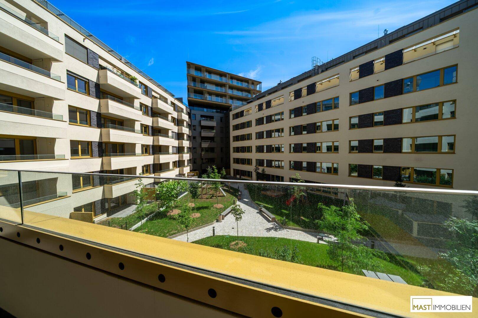 Blick vom Balkon auf einen begrünten Innenhof mit modernen Gebäuden und gepflegten Grünflächen.