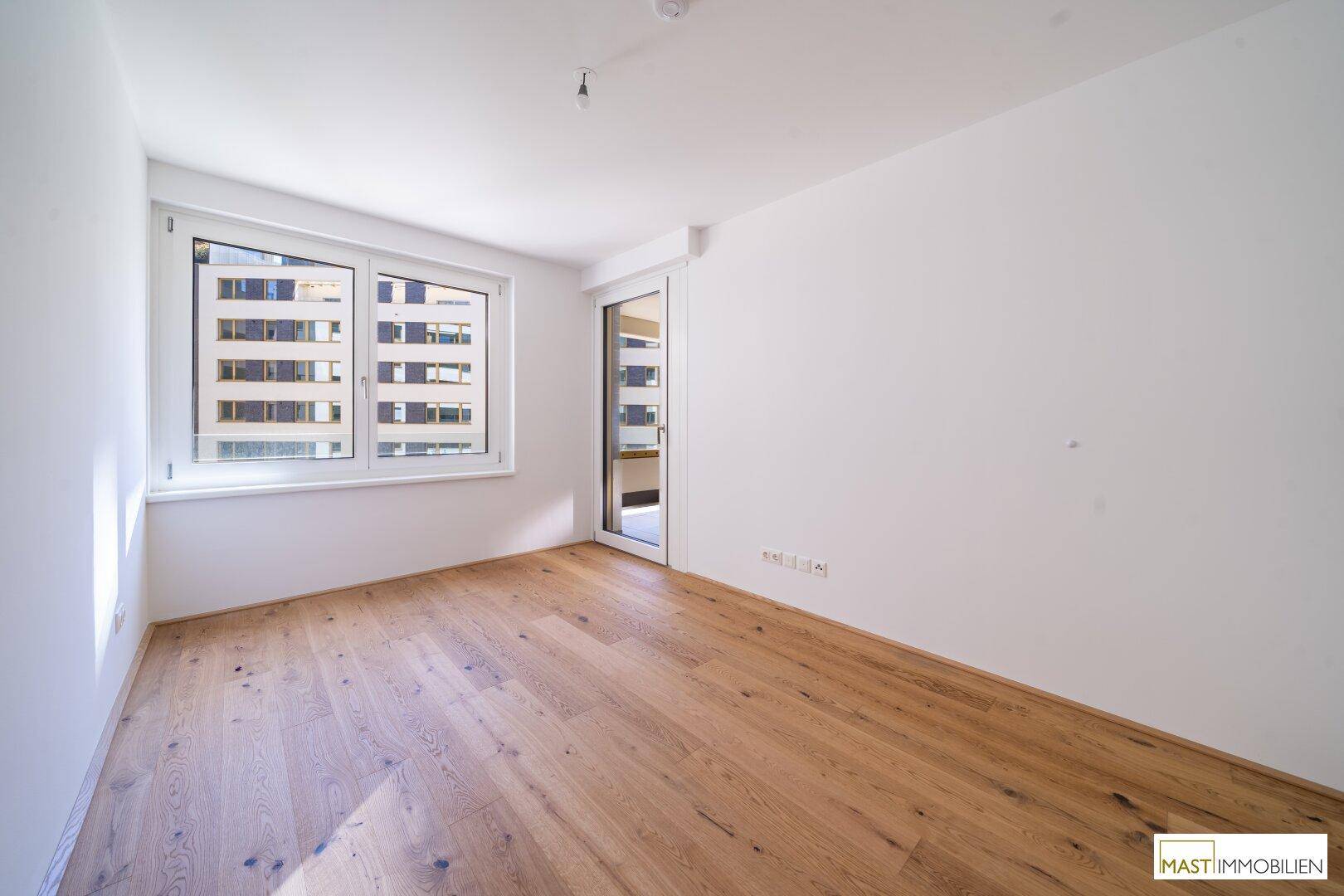 Helles Schlafzimmer mit Eichenparkettboden und großem Fenster mit Blick auf die Stadt.