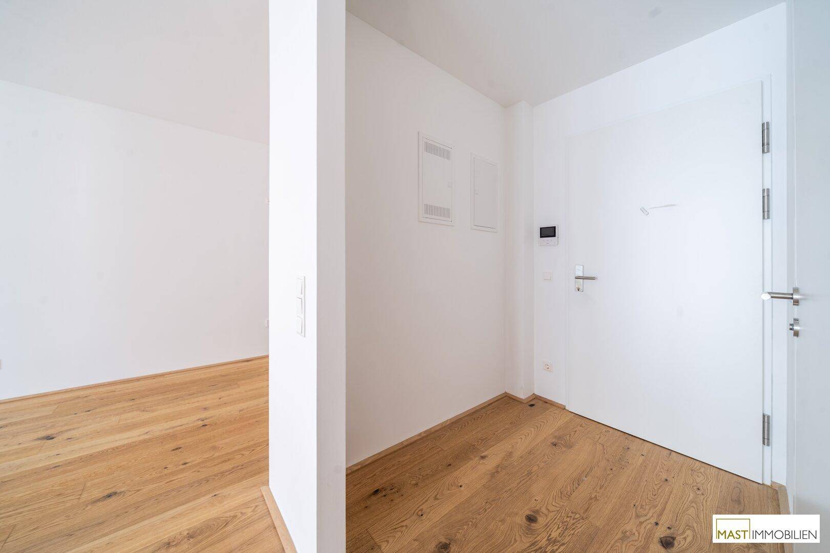 Heller Flur mit Parkettboden und weißer Tür, der zu den weiteren Räumen der Wohnung führt.