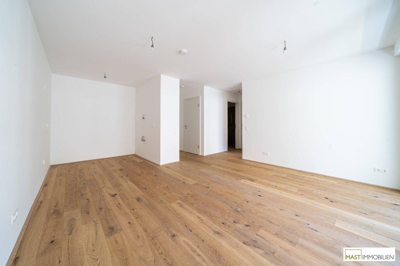 Heller Eingangsbereich mit hochwertigem Parkettboden und weißen Wänden in einem modernen Neubau.