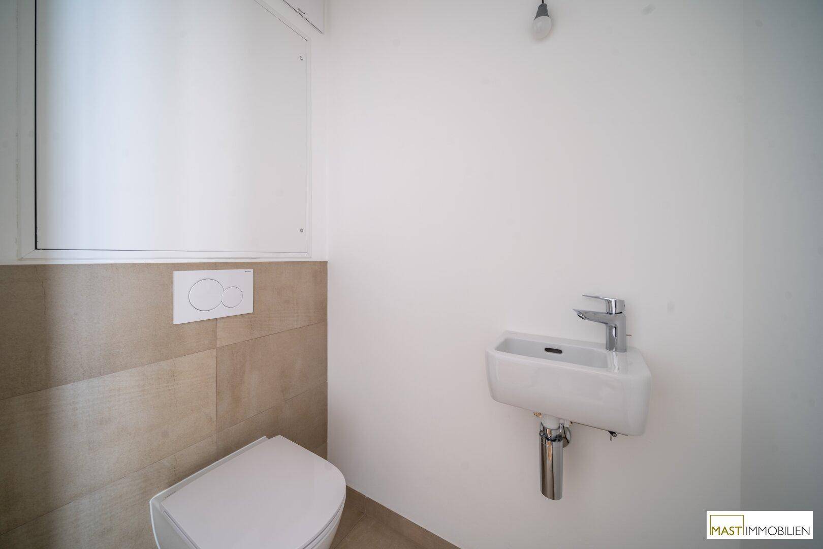 Separates Gäste-WC mit Wand-WC und kleinem Handwaschbecken, ausgestattet mit modernen Fliesen.
