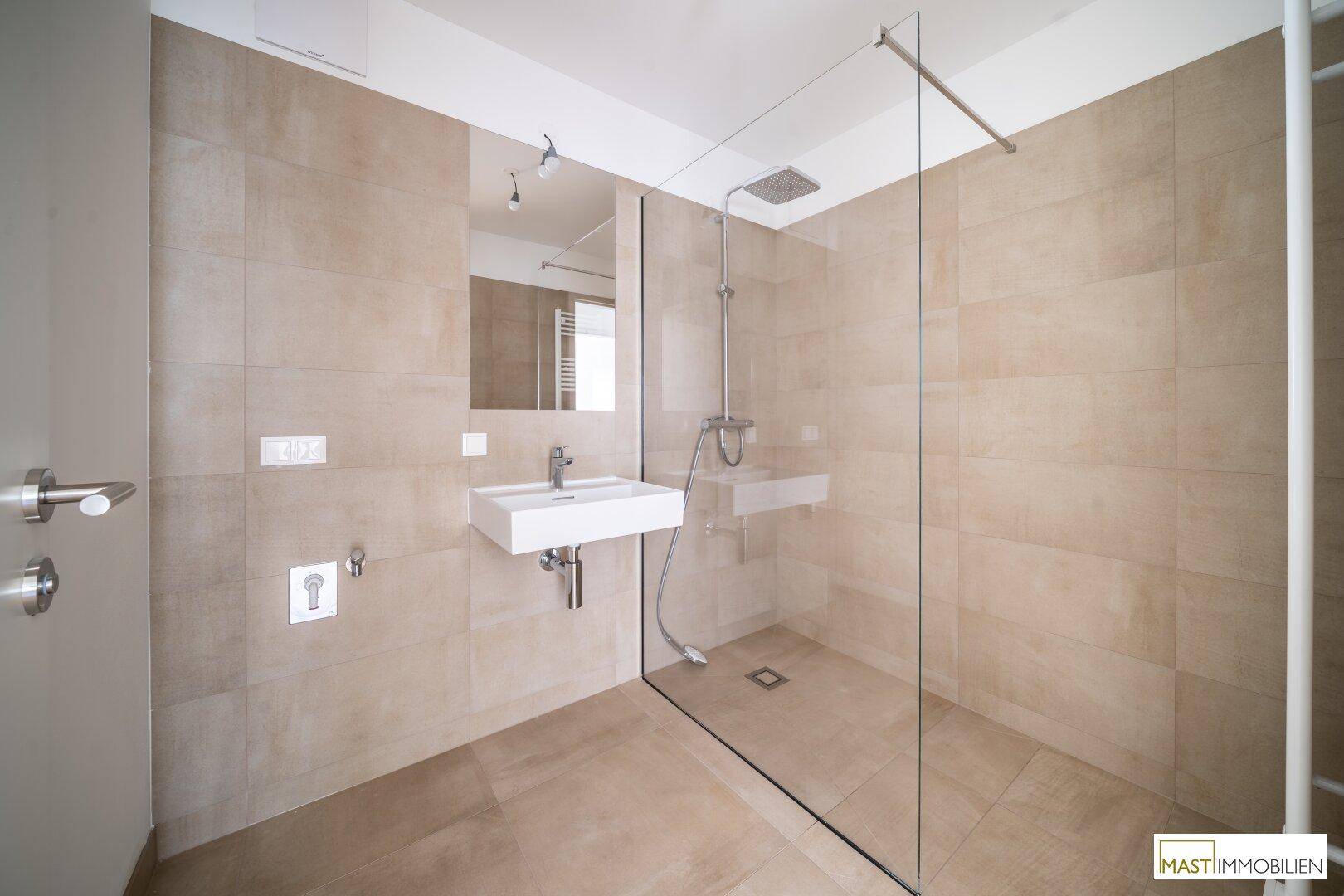 Elegantes Badezimmer mit beigefarbenen Fliesen, modernem Waschbecken und großer Regendusche.