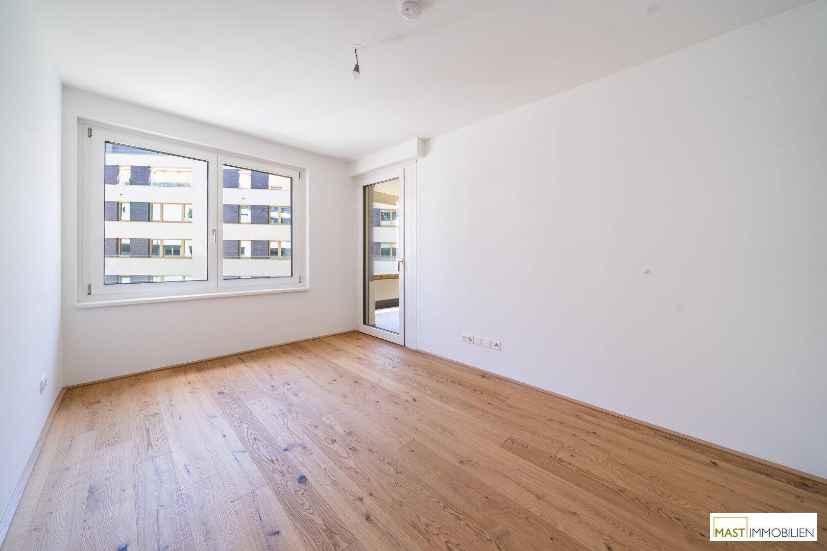 Geräumiges Schlafzimmer mit Holzboden, großen Fenstern und direktem Zugang zum Außenbereich.