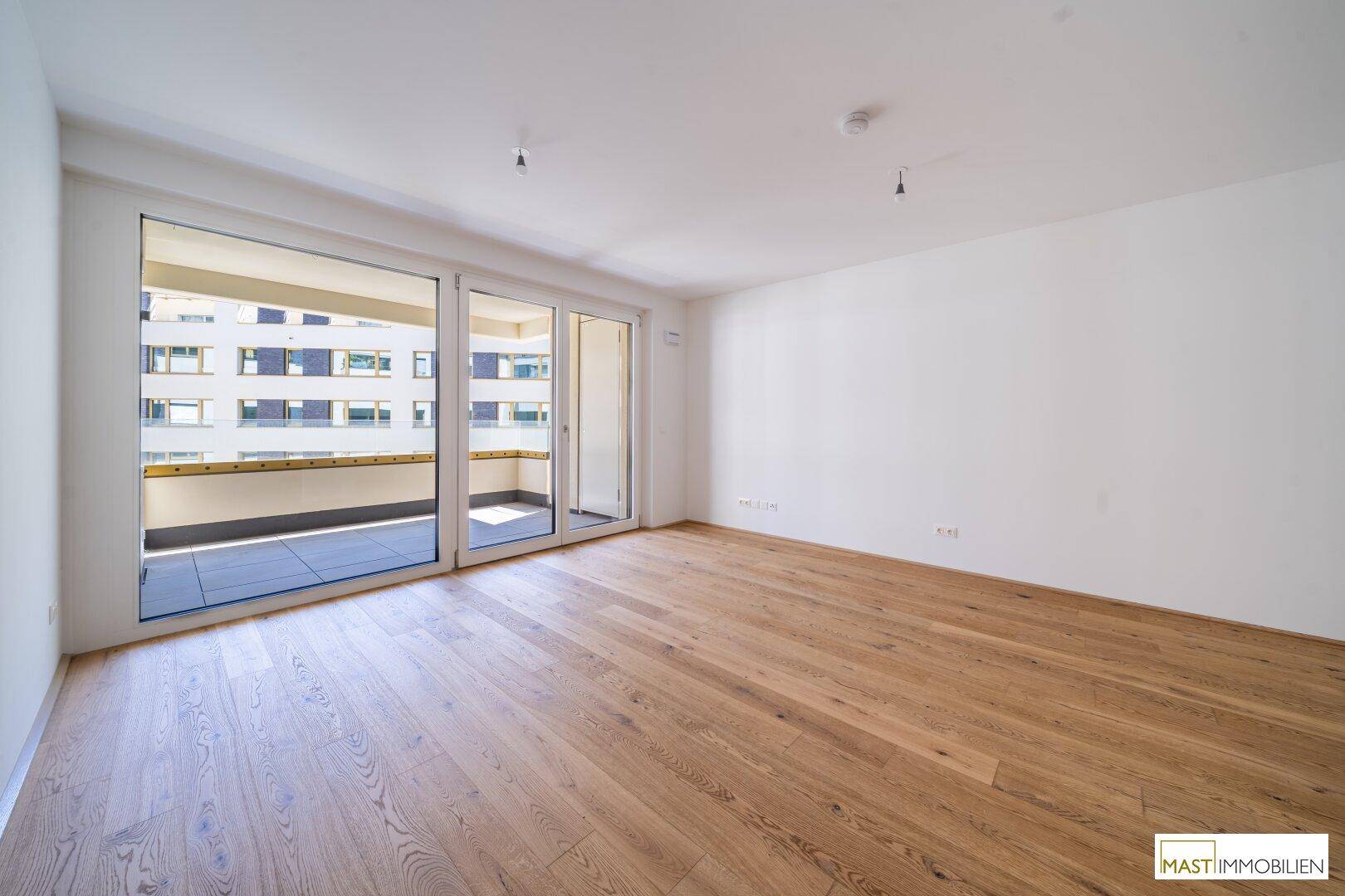 Heller Wohnraum mit hochwertigem Parkettboden und direktem Zugang zu einem sonnigen Balkon.