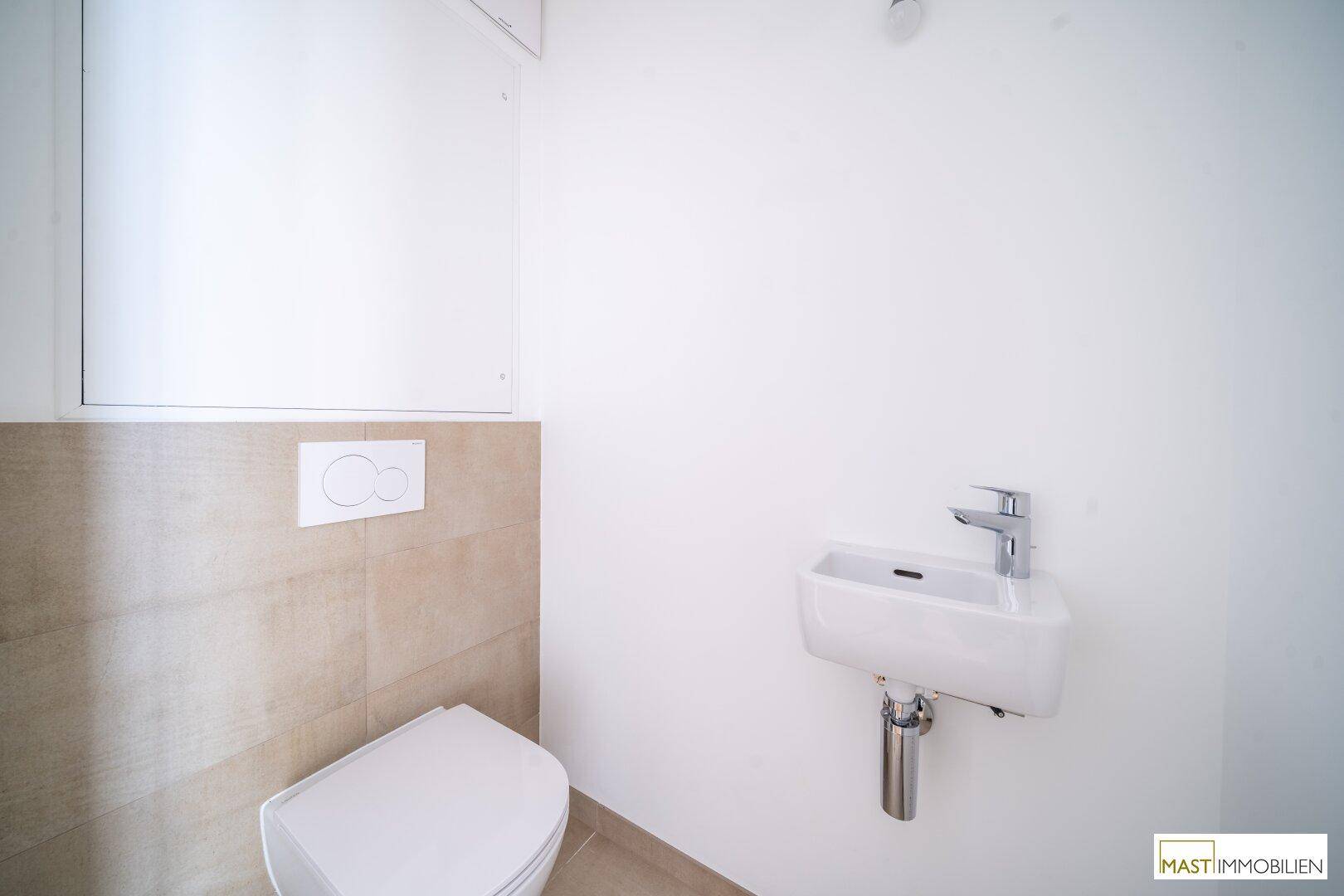 Separates Gäste-WC mit Wand-WC und kleinem Waschbecken, in modernem Design gehalten.