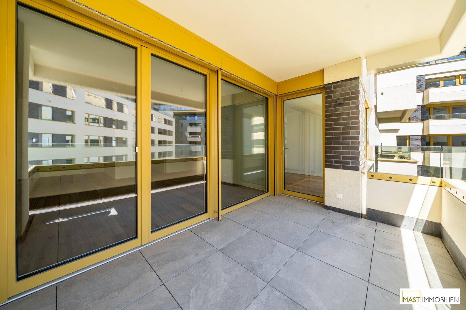 Geräumiger Balkon mit Fliesenboden, Glasgeländer und sonnigem Ausblick auf die moderne Umgebung.