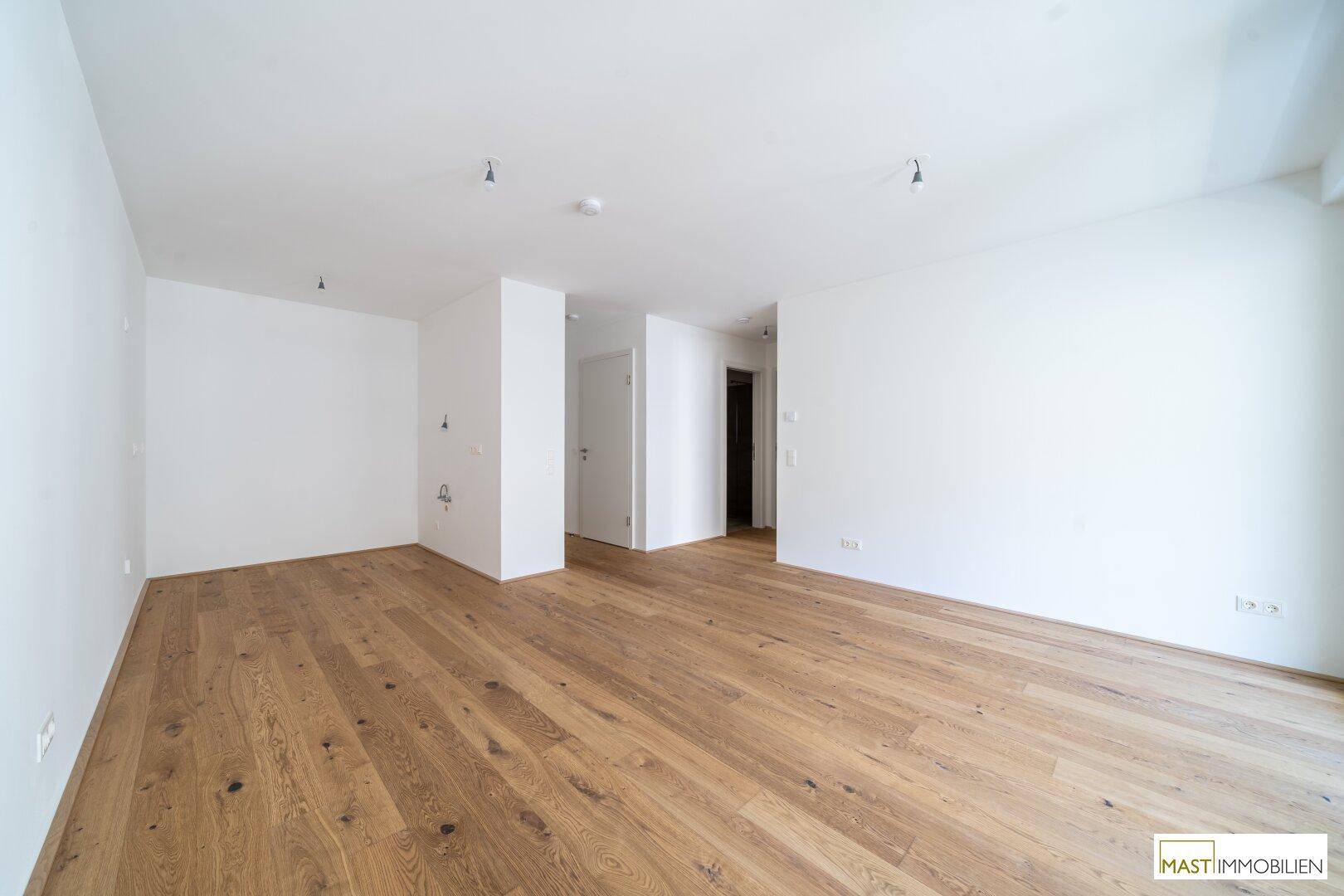 Geräumiges, leeres Zimmer mit hellem Parkettboden und weißen Wänden, bereit zum Einzug.