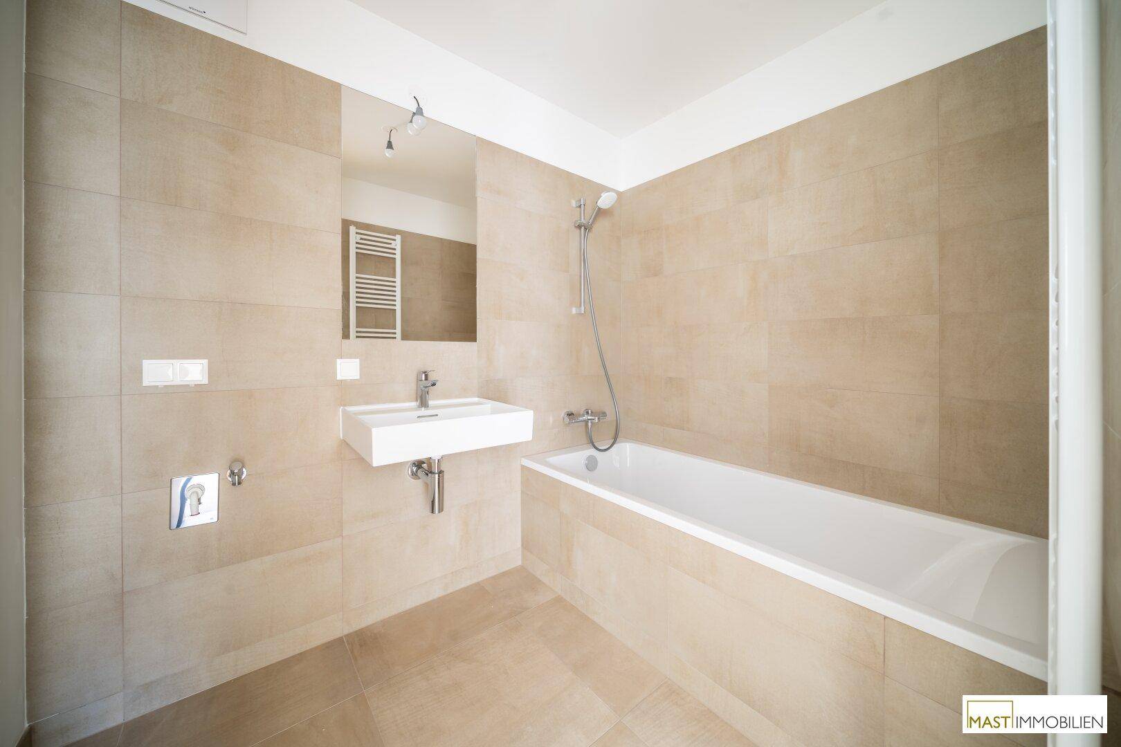 Modernes Badezimmer mit Badewanne, Waschtisch und beigefarbenen Fliesen, in neuwertigem Zustand.