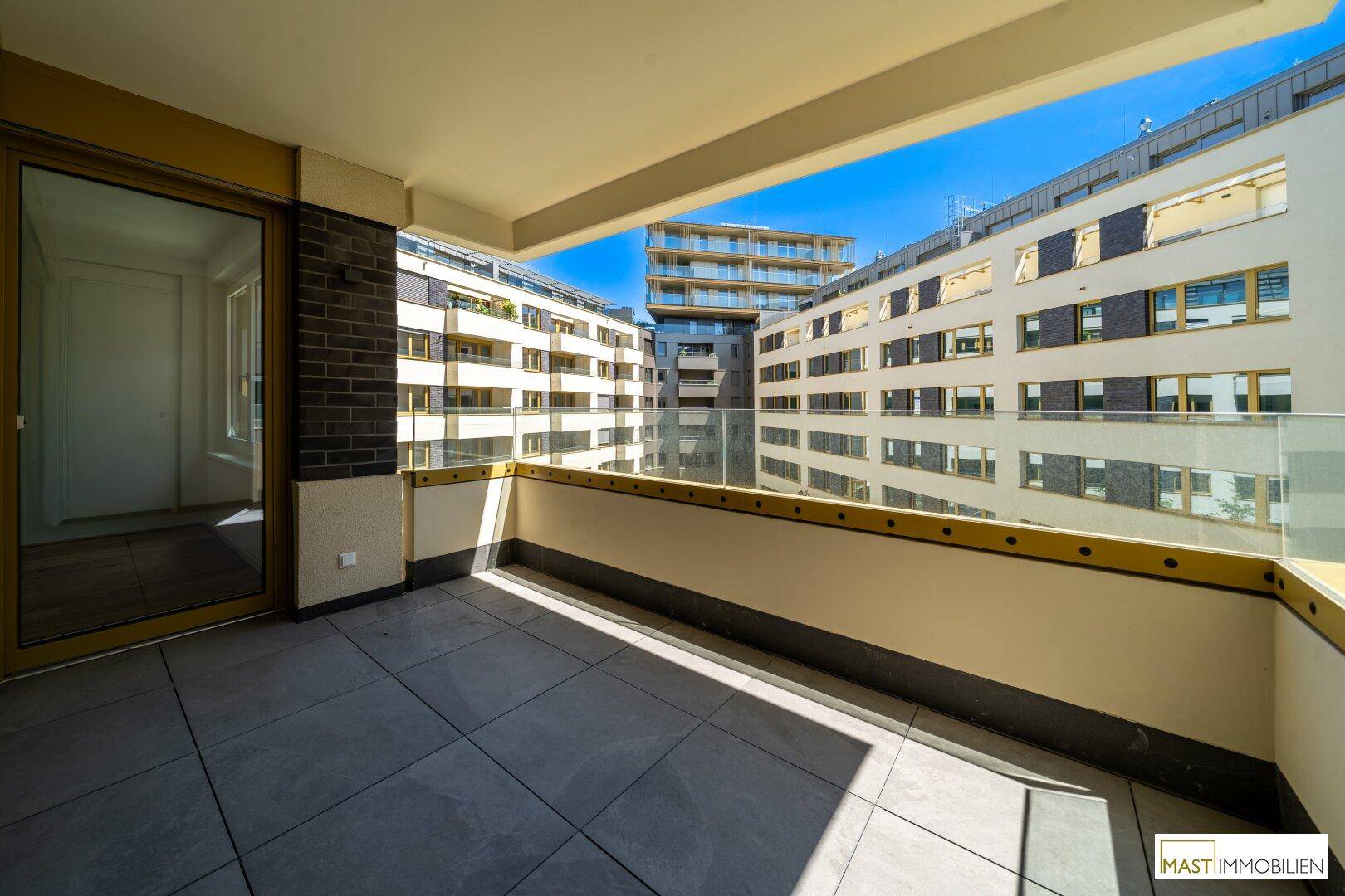 Heller Balkon mit Fliesenboden und Panoramablick auf die umliegenden Neubauten und den Himmel.