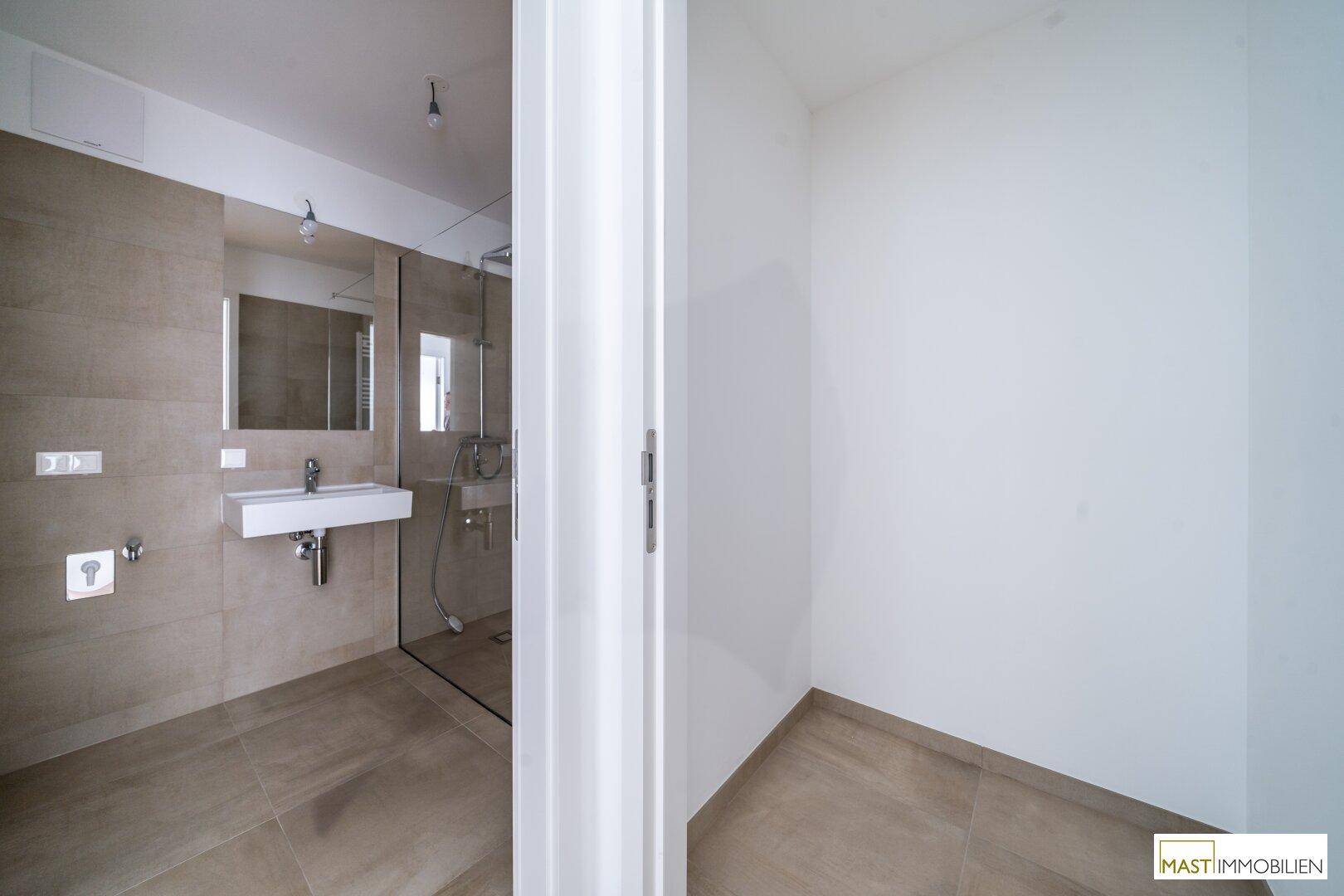 Modernes Badezimmer mit beigefarbenen Fliesen und einer begehbaren Dusche, teilweise sichtbar.